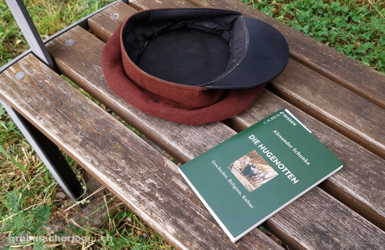 buch uber die geschichte der hugenotten und hut auf einer sitzbank